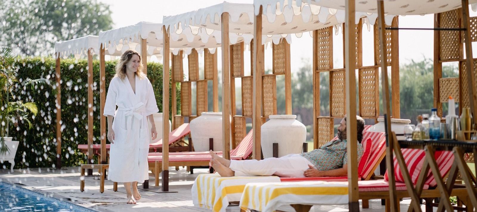 A man seating beside a swimming pool and a woman walking beside it at Surpura Bagh.