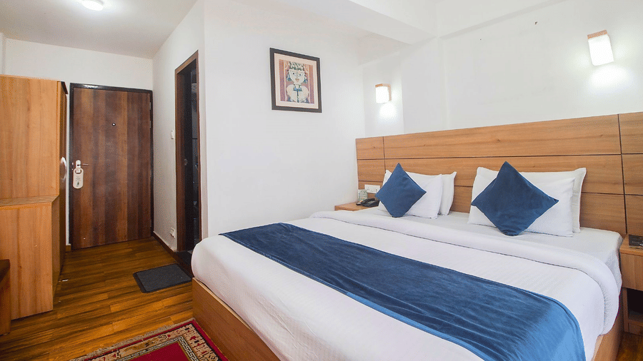 The Deluxe Room with double bed, framed art work on the wall, TV, Wardrobe, Dustbin, Table and desk with two water bottles on the top at  Central Heritage Resort and Spa (Formerly Fortune ITC Resort) The Mall Ro