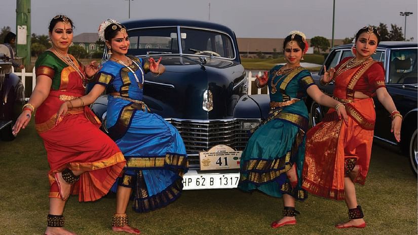 A group of classical dancers posing next to an antique car - Karma Lakelands.