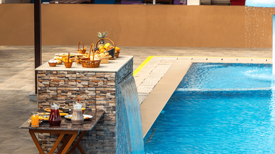 Close-up of refreshments served on a table next to the resort swimming pool with a waterfall feature - Nature Trails Ashoka Resort Hampi