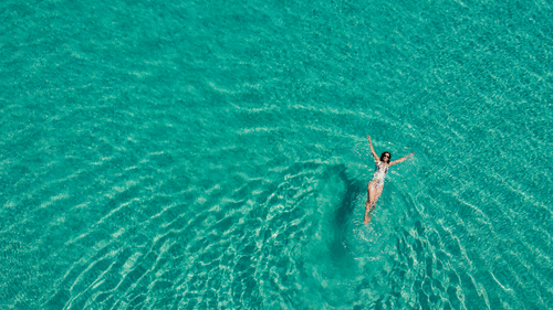 Aerial view of a person swimming alone in turquoise waters, with ripples surrounding her.