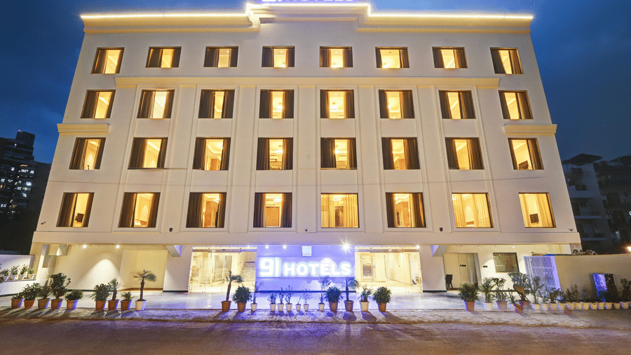 A brightly lit facade of Hotel 91 Privé, Gurugram, during the late evening hours with each window of the hotel emitting warm golden lights.