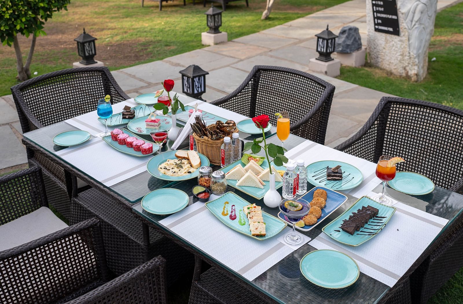 A neatly set outdoor dining table. The table is set with plates, glasses, and various dishes.