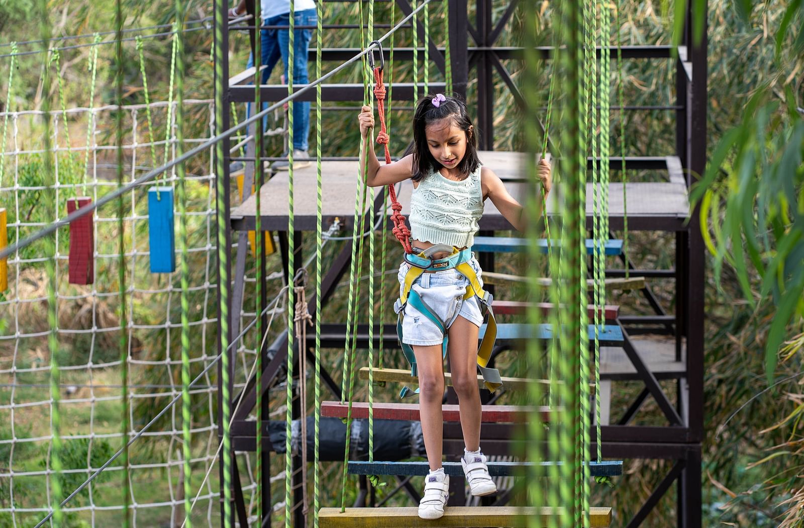 A person on a ropes course, an outdoor adventure structure and surrounded by trees and greenery.