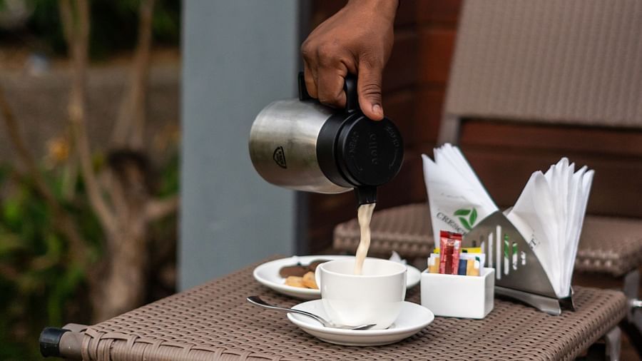 A person pours tea into a cup while snacks and napkins are arranged neatly on the cottage room table in the Crescent Spa & Resort, Indore 