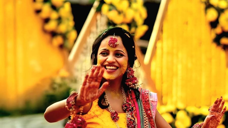 A woman in traditional Indian attire sits on the ground in a decorated outdoor setting, surrounded by yellow flowers and festive elements