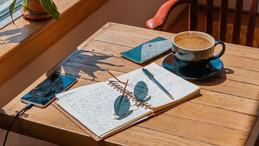 A cup of coffee a diary glasses and mobile phones on a table at a cafe