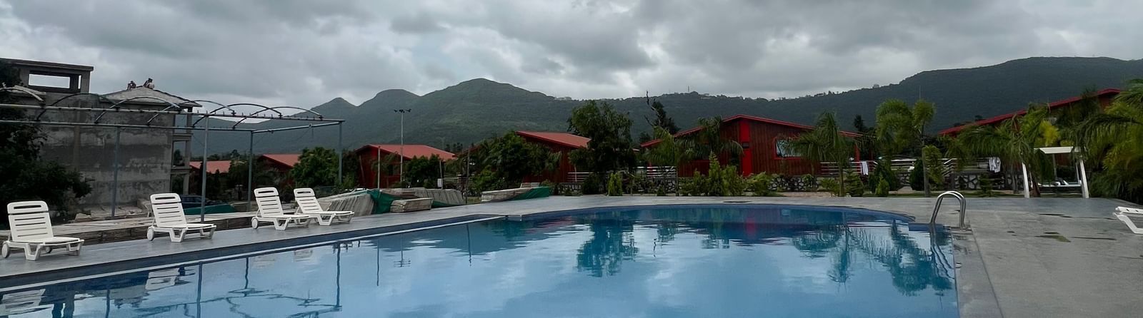 Outdoor swimming pool area at Daksh The Valley Resort, Saputara. Wide view of the water and surrounding paved deck.