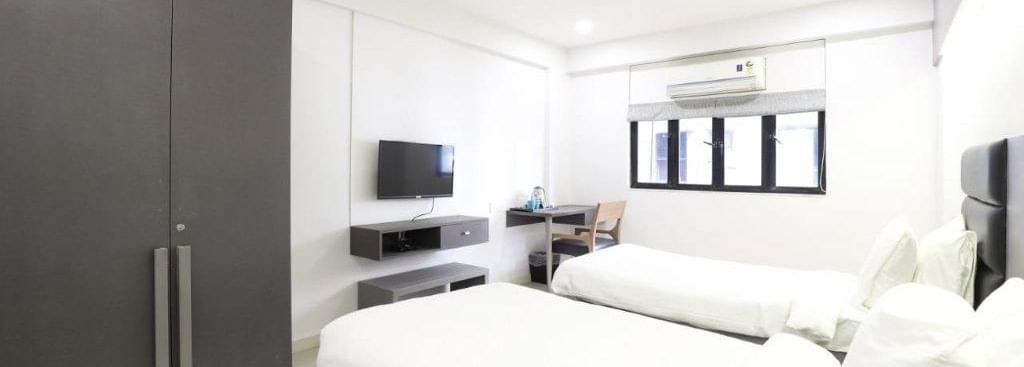 Corner view shot of the Premium Twin Room at Pravasa Ahmedabad featuring bright and minimalist interiors along with a wardrobe in the corner.