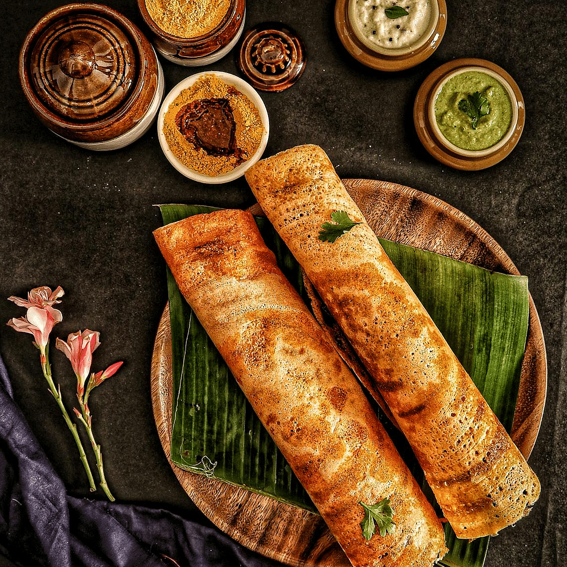 Image of two dosas on a table with chutneys on the side.