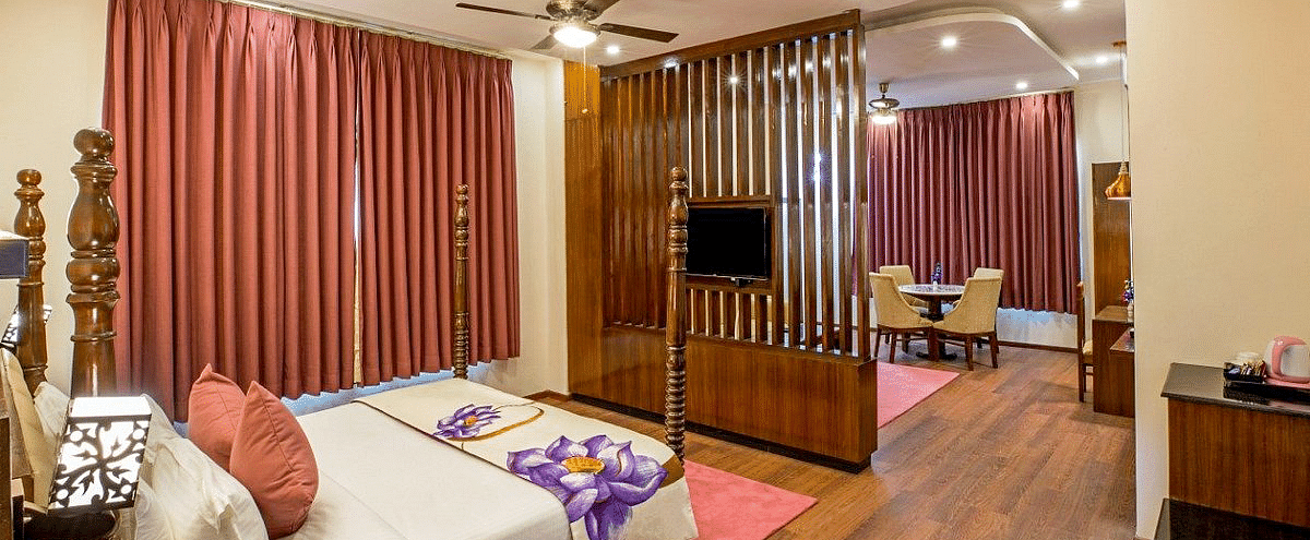 Corner view angle of the Suite at Regenta Inn DLS with a wooden partition in the middle with a television mounted over it.