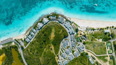 Aerial view of Tamarind Hills Resort in Antigua, nestled between lush greenery and turquoise Caribbean waters along a white-sand beach.