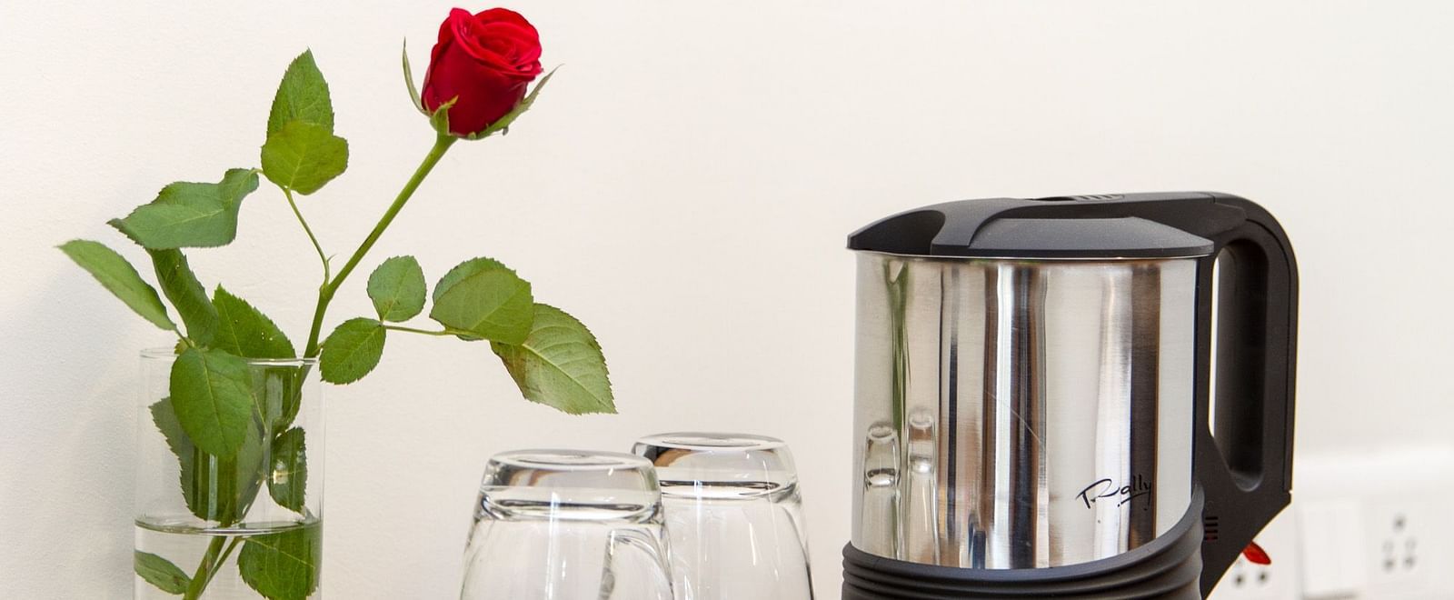A kettle and glasses placed on a tray and a small vase with a single red rose beside it - Sanctum Suites Whitefield, Bangalore