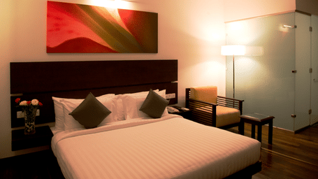 A bedroom at Springs Hotel & Spa, J.C. Road with king size bed, side tables, lamps, wall art above the headboard, and chair.
