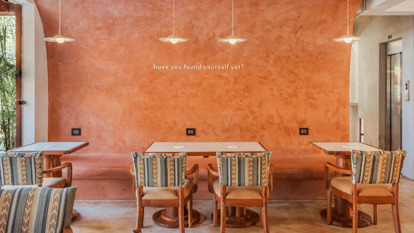Book direct and get 31% off at Unseen Boutique Hotel Assagao Goa featuring a cozy seating area with two patterned armchairs a checkered rug and warm string lights on a wooden ceiling.
