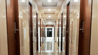 A brightly lit hotel hallway with a shiny, reflective floor, leading past a row of dark wooden doors | A & M Rooms and Residences