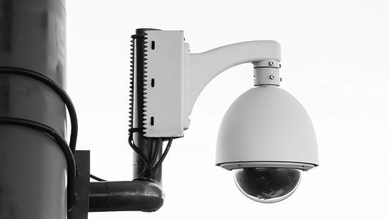 A black and white close-up image of a dome-shaped security camera mounted on a pole.
