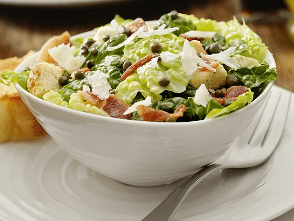 A salad presented in a white bowl with a sandwich in the background - S Hotel Kingston, Jamaica
