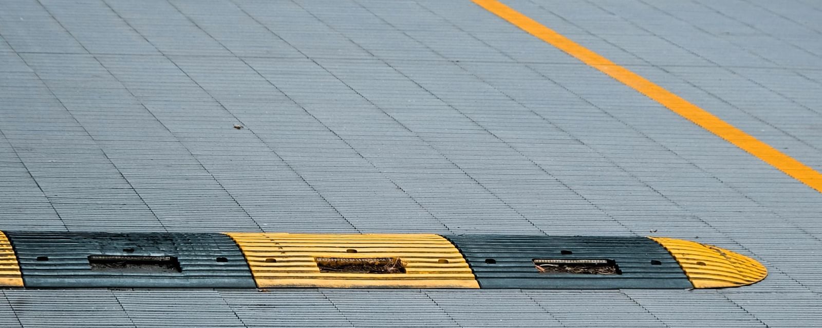 Close-up of a grey parking area with yellow and black speed bumps and a yellow line marking.