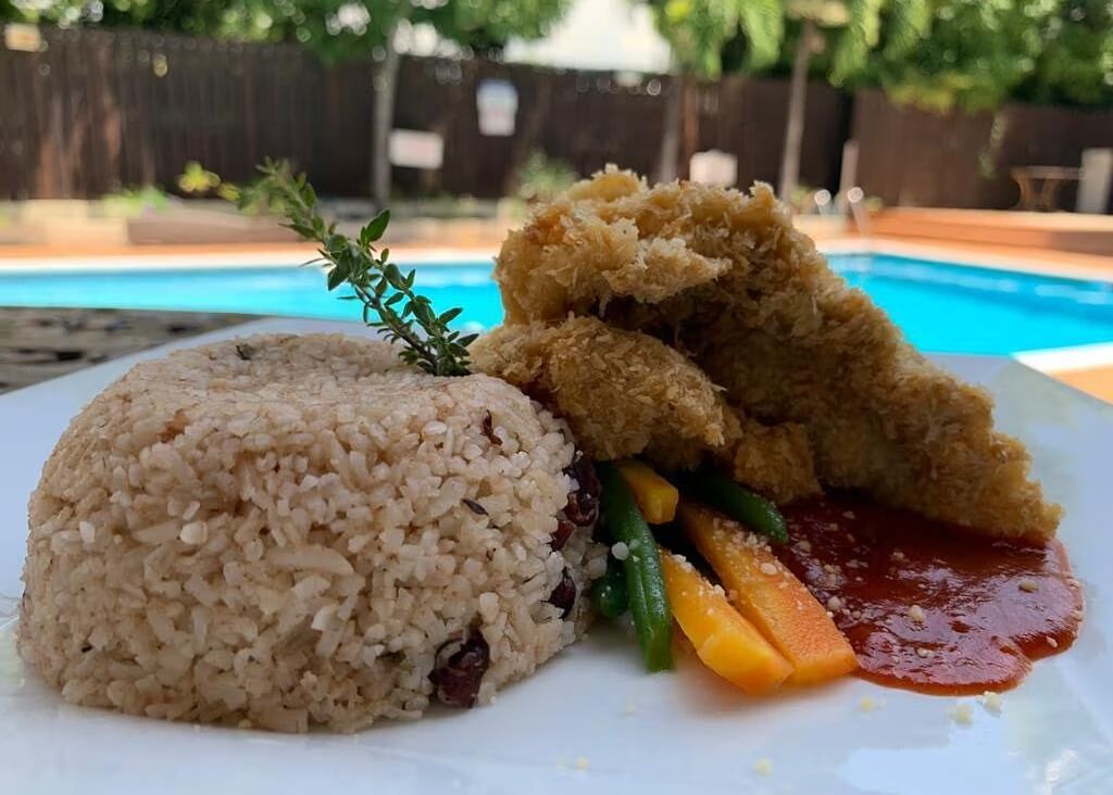 A plate with rice and a piece of fried fish or chicken, served by a swimming pool | Altamont Court, Jamaica