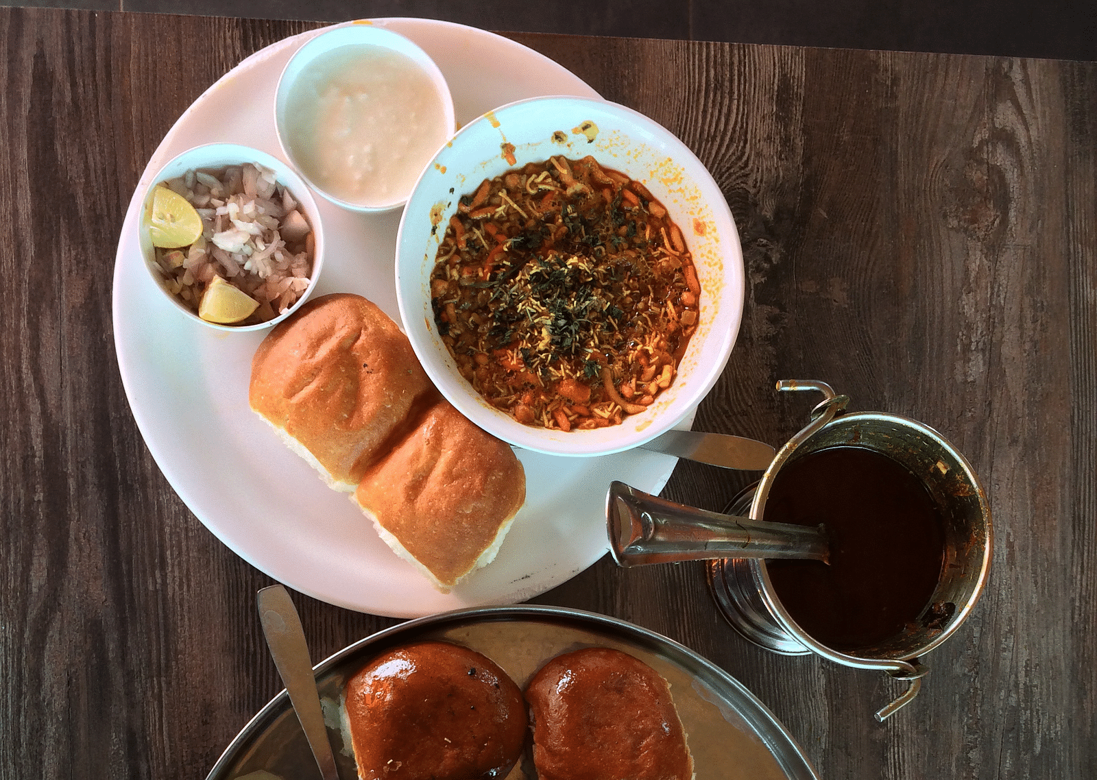An aerial view of a breakfast spread that includes misal pav with onions, curd and other items.