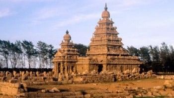 A stone temple reflected in a water, with carvings and trees in the background.