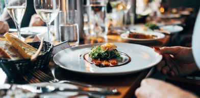 A close-up of a plated dish on a restaurant table with cutlery, glasses, and bread placed around it.