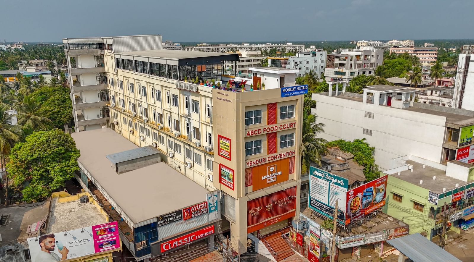 Aerial view of Monday Hotels Amalapuram Heights surrounded by other buildings and trees.