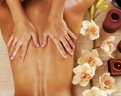 Hands massaging a person's back in a spa environment, with flowers and other spa elements arranged nearby.