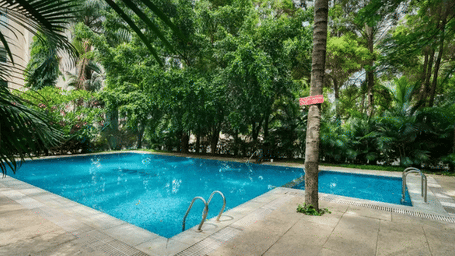 Outdoor swimming pool surrounded by lush trees and a paved deck at Featherlite Evoma Hotel.