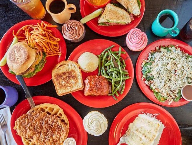 Top view of Spread of food like green vegetables, bread, burger, fries, waffles and other beverages placed on red plates and cups 