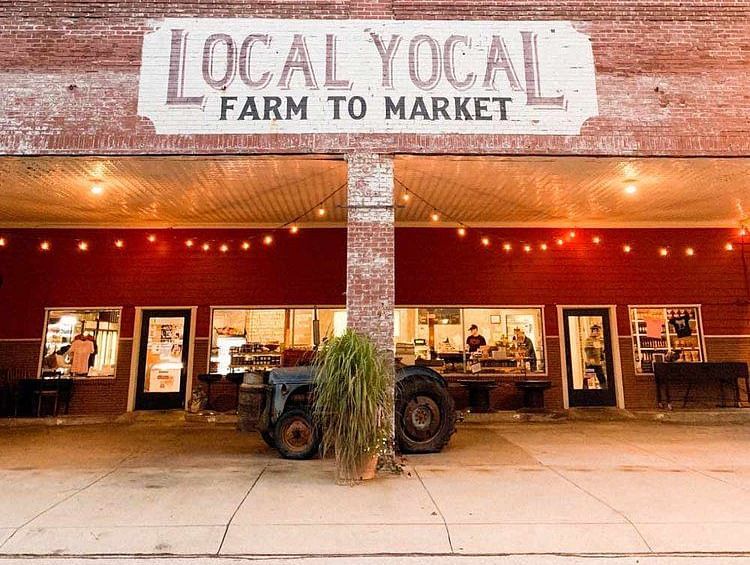 Exterior view of a market place named local yocal farm to market with a red wall on the outside and fairy lights as  decoration.