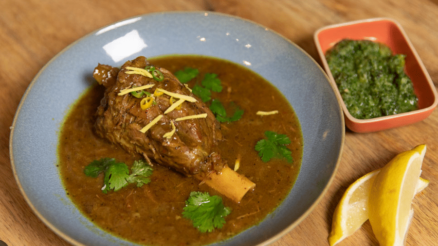 Top angle view of a plate of Nalli Nihari in rich gravy, accompanied by chutney and lemon slices.