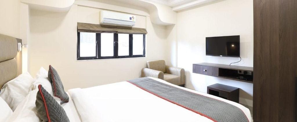 A wide-angle shot of the Premium Room at Pravasa Stay, Ahmedabad (Alba Premier), featuring a double bed along with a wall-mounted television.