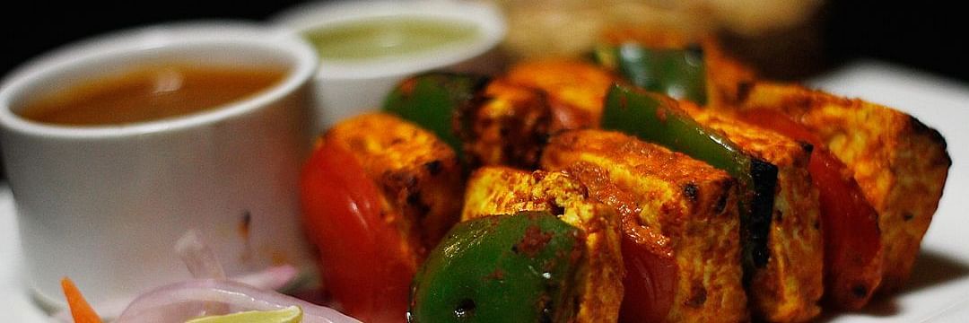 Paneer Tikka plated in a white dish with red and green chutney