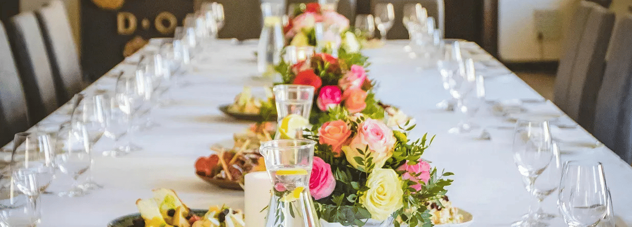 A banquet table set with white linen, flowers, and glassware, prepared for dining or an event.