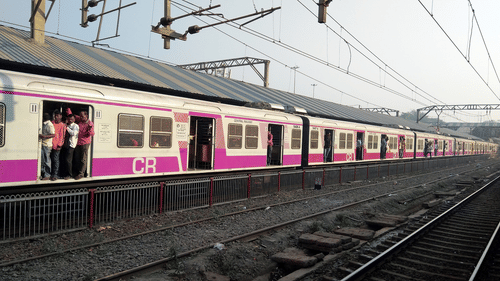 Pink and white local train at a station platform, with passengers standing near the doors.