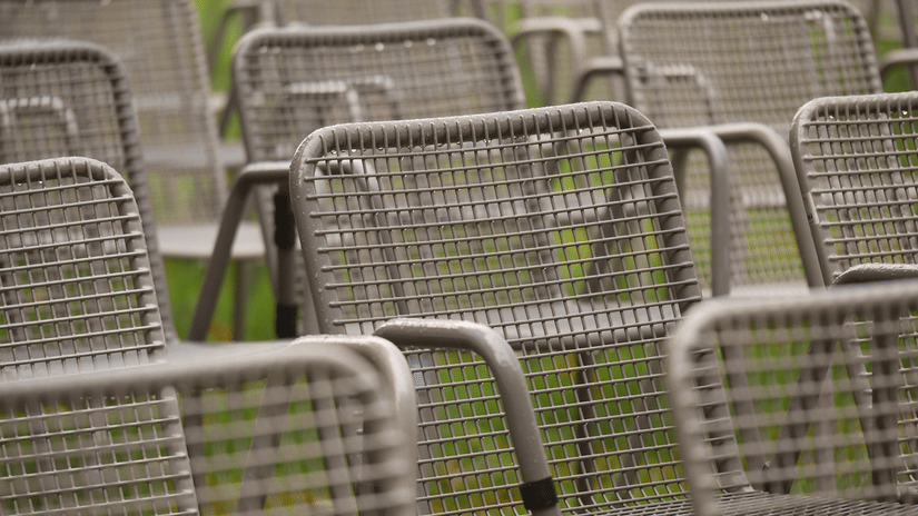 Rows of empty grey metal mesh chairs arranged closely together in an outdoor or park setting.