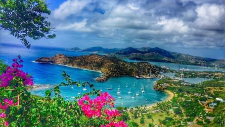 Stunning panoramic view of a bay with turquoise water, lush green hills, and vibrant pink flowers - Tamarind Hills Resort and Villas - Antigua
