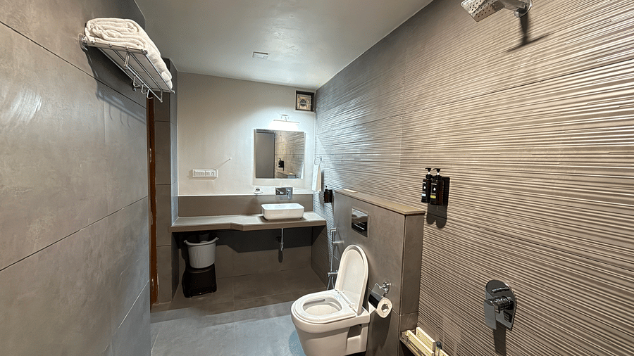 A sleek bathroom with textured grey wall tiles, a modern toilet, and a clean vanity area - Daksh The Nirvana Retreat, Pavagadh