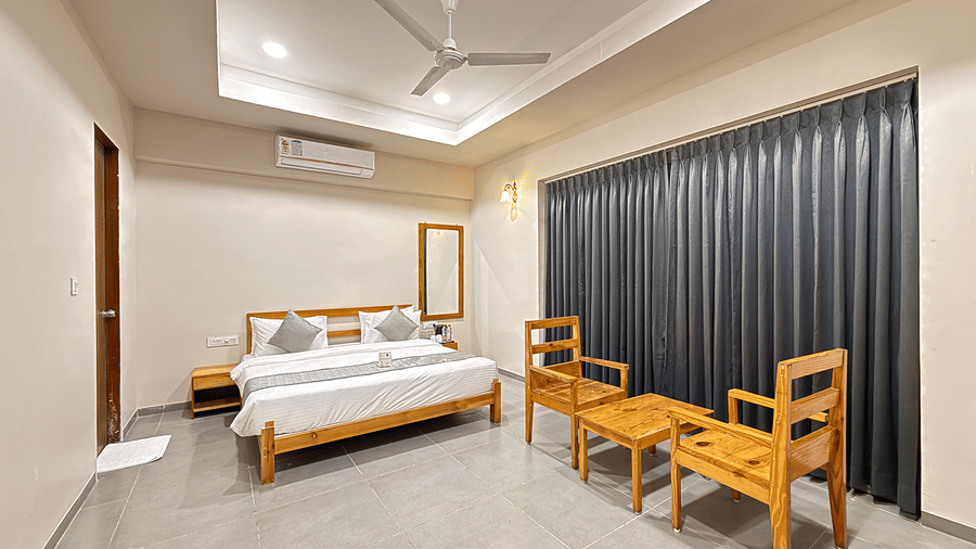 A minimalist bedroom featuring a double bed, wooden furniture, and floor-to-ceiling grey curtains - Daksh The Nirvana Retreat, Pavagadh