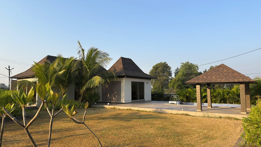 A wide view of the resort grounds featuring green lawns, palm trees, and modern cottage buildings under a clear sky - Daksh The Nirvana Retreat, Pavagadh