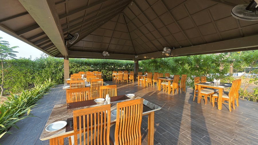 A large, open-air dining pavilion with numerous wooden tables and chairs set for guests - Daksh The Nirvana Retreat, Pavagadh
