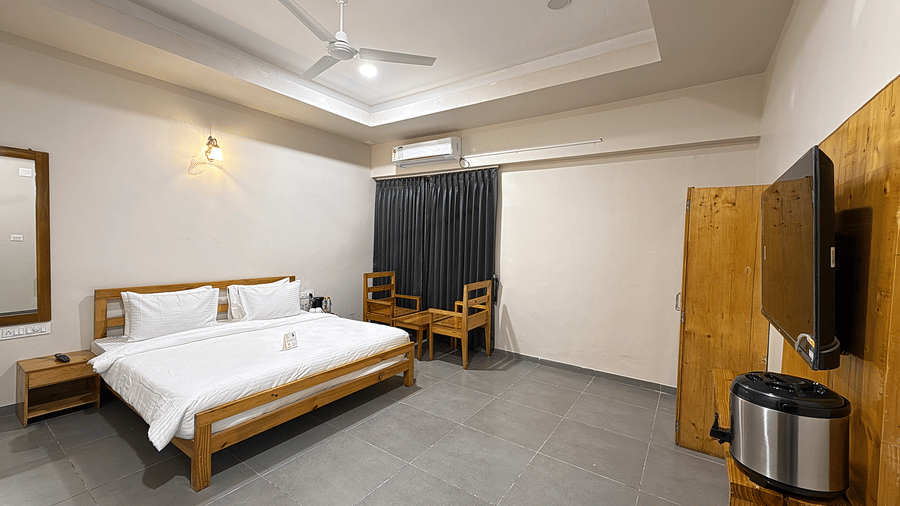 A wide-angle view of a luxury suite featuring a large bed, wall-mounted TV, and polished grey flooring - Daksh The Nirvana Retreat, Pavagadh