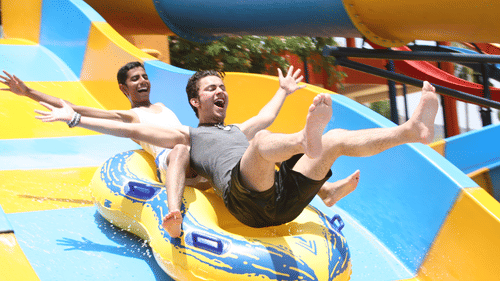 Two excited people riding an inflatable tube down a thrilling water slide, their hands raised as they glide over the colourful surface - The Black Thunder