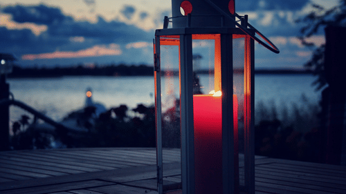 a candle inside a lamp with a lake and the evening sky in the background 