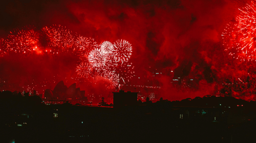 Bright red fireworks lighting up the night sky above a dark city skyline.