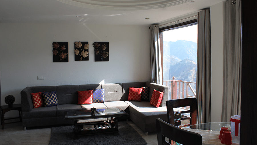 A sofa set in the living room with three frames on the wall, beside a huge glass window - Homestay in Himachal Pradesh