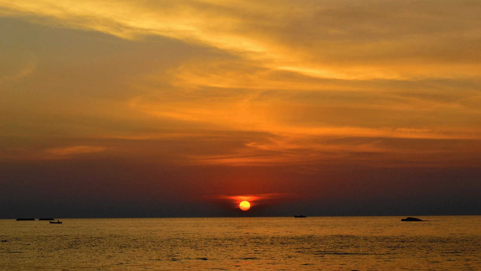 The sun sets over the ocean creating a vibrant orange and yellow sky, looked over from the shore of one of the best South Goa tourist places.
