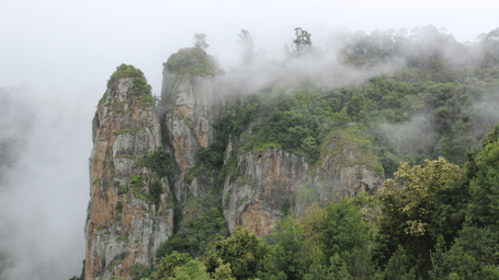 An overview of Pillar Rocks in Kodaikanal with mist hanging low on it.